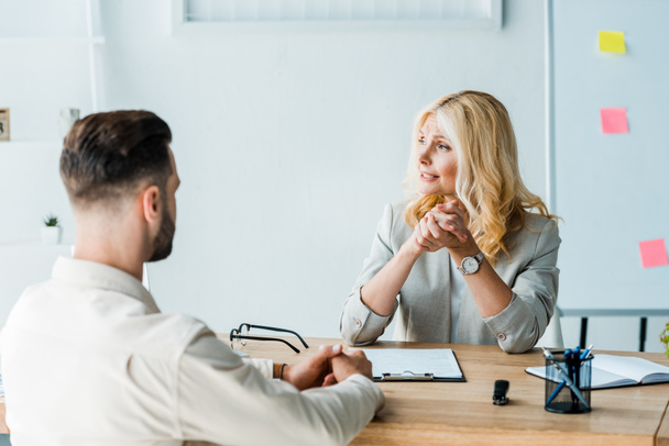 selective focus of blonde recruiter sitting with clenched hands bearded man  - Photo, Image