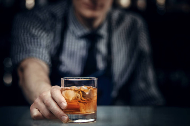 Barman holds out glass of whiskey with ice to male visitor. Concept rest in bar - Photo, image