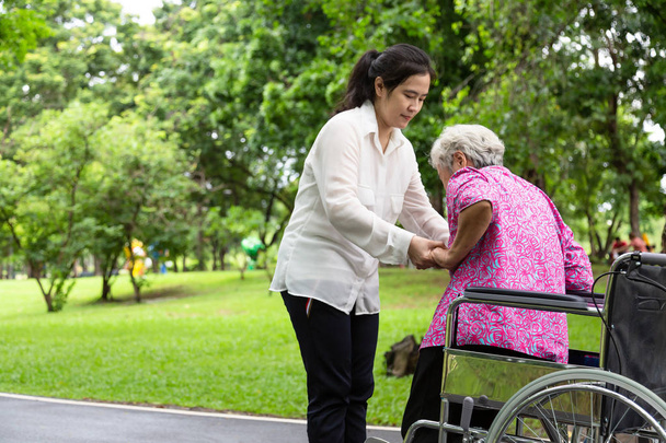 Ženská kastrální podpora asijského nebo mladého ošetřovatele, která pomáhá starší ženě vstát ze venkovního vozíčku ve venkovním parku, trpělivá matka se svou dcerou v letní zelené přírodě, rodině, starším pojetí péče - Fotografie, Obrázek