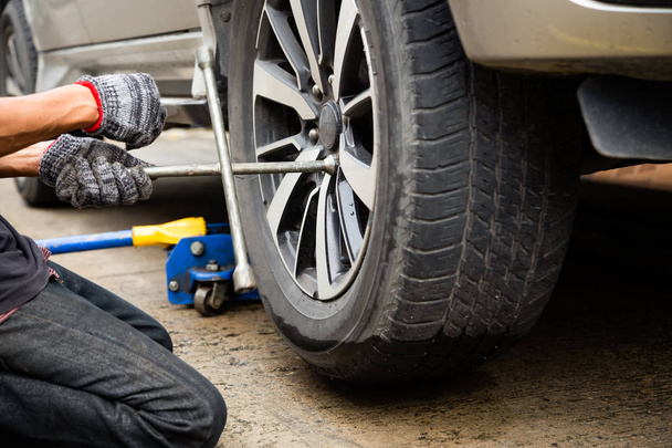 Mladý muž mechanik nosí rukavice, auto opravy, výměna pneumatiky pomocí klíče opravit auto kolo ploché pneumatiky na silnici, doprava a cestování koncepce - Fotografie, Obrázek