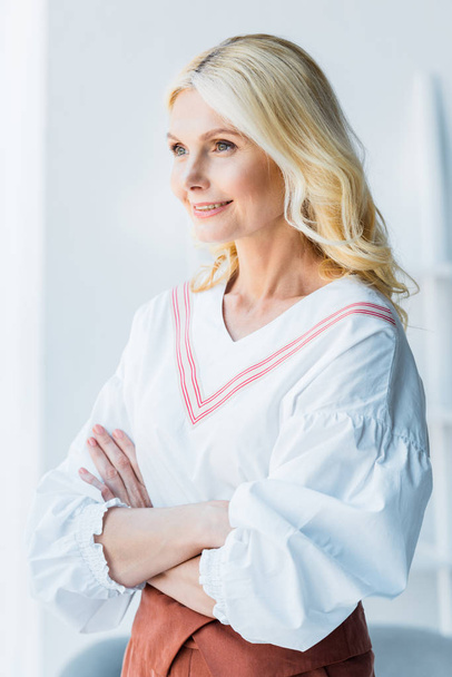happy blonde woman standing with crossed arms in office  - Fotografie, Obrázek