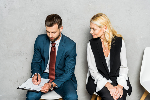 attractive blonde woman looking at clipboard while man writing in office  - Foto, Bild