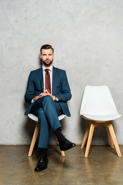 handsome bearded man sitting with crossed legs on chair in office  - Фото, зображення