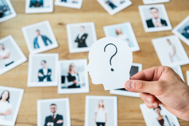 cropped view of man holding paper with human head and question mark near photos  - Photo, Image