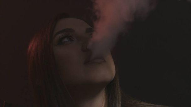 Beautiful sexy brunette girl with bright makeup exhaling smoke from her mouth on black background, bad habits concept. Action. Portrait of young woman smoking hookah. - Fotoğraf, Görsel
