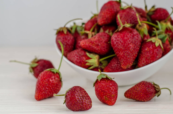 Fresh summer ripe strawberries in a white plate on a white woode - Fotó, kép