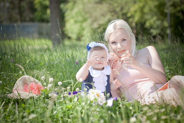 Beautiful blond hair mother and daughter are sitting in the grass - Photo, Image