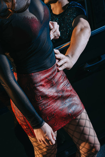 Freier berührt verführerische Prostituierte in rotem Rock, die in der Nähe von Auto steht  - Foto, Bild