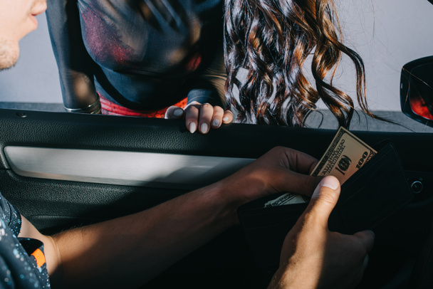 cropped view of man in car holding wallet with cash near prostitute - Photo, Image