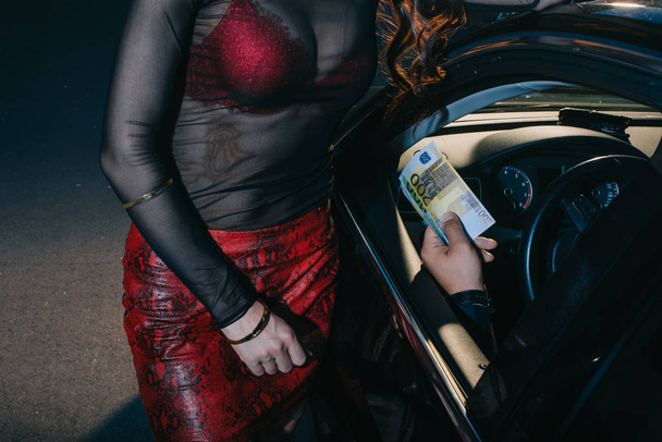 bijgesneden beeld van de klant in de auto geven eurobankbiljetten aan prostituee  - Foto, afbeelding