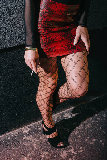 recortado vista de sexy prostituta en rojo falda de pie cerca de la pared con cigarrillo
  - Foto, imagen