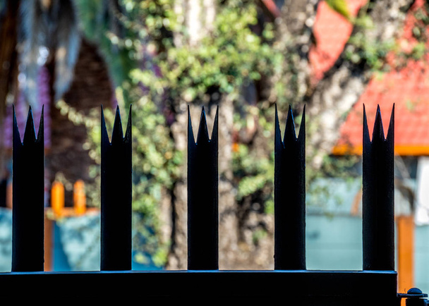 Una valla de metal con pinchos para la seguridad del hogar, silueta contra una imagen de fondo fuera de foco en formato de paisaje con espacio de copia
 - Foto, Imagen