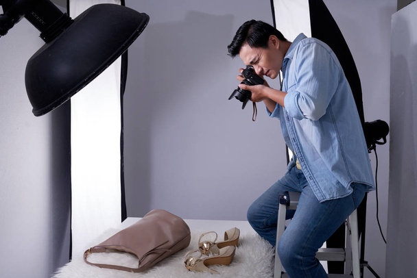 Азиатский юноша фотографирует каблуки и сумки в профессиональной студии
 - Фото, изображение