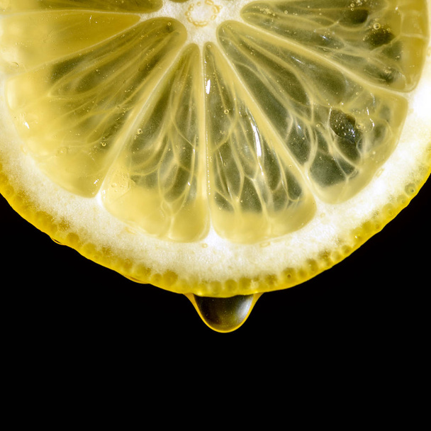 slice of lemon with a drop of juice on a black background close-up - Fotoğraf, Görsel