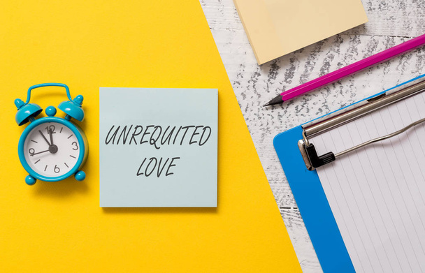 Word writing text Unrequited Love. Business concept for not openly reciprocated or understood as such by beloved Notepads clipboard colored paper sheet marker alarm clock wooden background. - Photo, Image