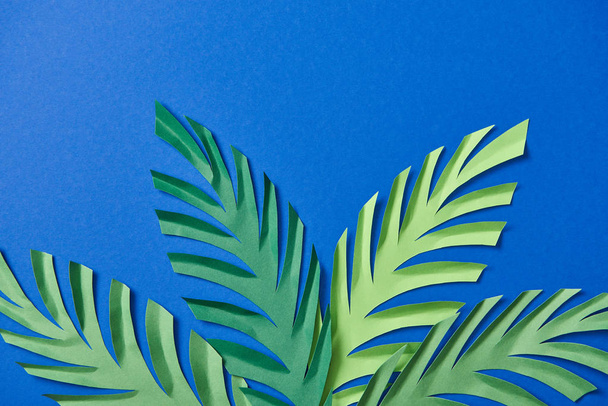 top view of green paper cut leaves on blue background with copy space - Φωτογραφία, εικόνα