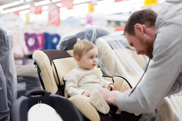 Young father with   small daughter choosing   car seat in   store of children's goods.  - Photo, Image