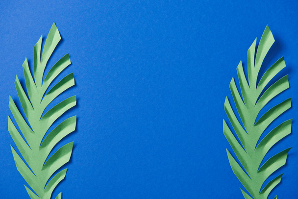 vista dall'alto delle foglie di carta verde tagliate su sfondo blu con spazio di copia
 - Foto, immagini