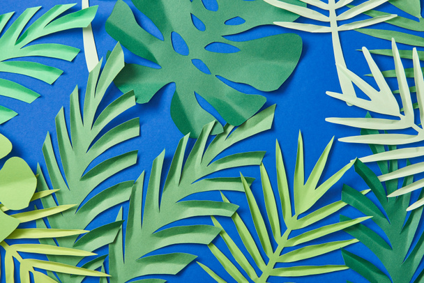 top view of green paper cut exotic leaves on blue background - Fotó, kép