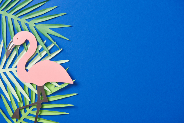 top view of green paper cut exotic leaves and flamingo on blue background with copy space - Photo, Image
