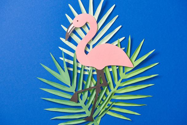 top view of green paper cut exotic leaves and flamingo on blue background - Photo, Image