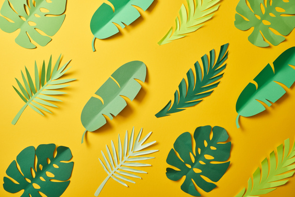 top view of paper cut green palm leaves on yellow background, seamless pattern - Photo, Image