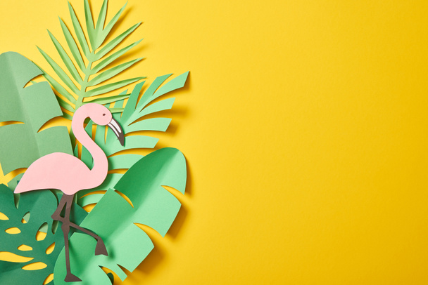 top view of paper cut green palm leaves and flamingo on yellow background with copy space - Foto, Imagen