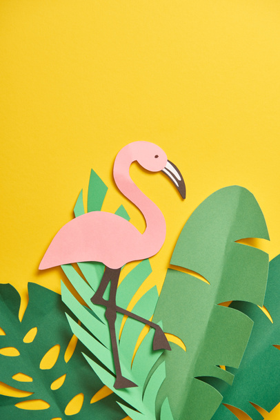 top view of paper cut green palm leaves and cute flamingo on yellow background  - Photo, Image