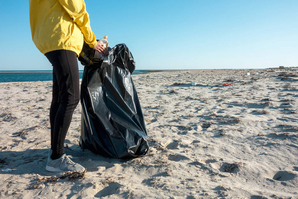 Kobieta zbierając śmieci i tworzyw sztucznych czyszczenia plaży z worka na śmieci. Działacz wolontariatu środowiskowego przeciwko zmianom klimatycznym i zanieczyszczeniom oceanów. - Zdjęcie, obraz