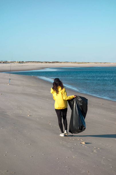Kobieta zbierając śmieci i tworzyw sztucznych czyszczenia plaży z worka na śmieci. Działacz wolontariatu środowiskowego przeciwko zmianom klimatycznym i zanieczyszczeniom oceanów. - Zdjęcie, obraz