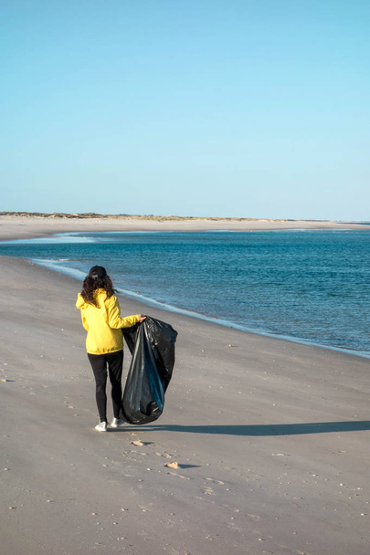 Женщина убирает мусор и пластик на пляже с помощью мешка для мусора. Эколог-волонтер против изменения климата и загрязнения океанов
. - Фото, изображение