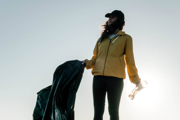 Nainen keräämässä roskia ja muovia siivoamassa rantaa roskapussilla. Vapaaehtoisympäristöaktivisti ilmastonmuutoksen ja valtamerten saastumisen torjunnassa
. - Valokuva, kuva