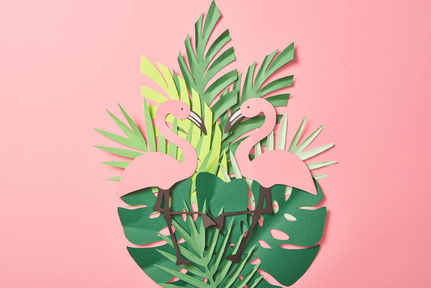 top view of paper cut flamingos on green palm leaves on pink background - Photo, Image