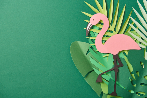 top view of paper cut palm leaves and pink flamingo on green background with copy space - Photo, Image
