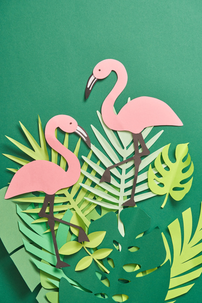 top view of exotic paper cut palm leaves and pink flamingos on green background with copy space - 写真・画像