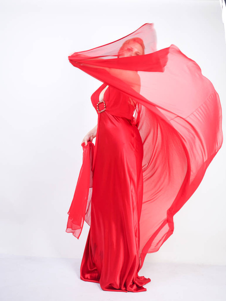 sexy blondýnka bělošská žena, která nosí dlouhé Rudé večerní šaty a pózová na bílém studiovém pozadí. ženská módní dívka s tělem plus i. stojící v elegantních stranické šatech. - Fotografie, Obrázek