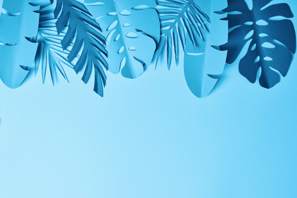 top view of blue exotic paper cut palm leaves on blue background with copy space - Fotografie, Obrázek
