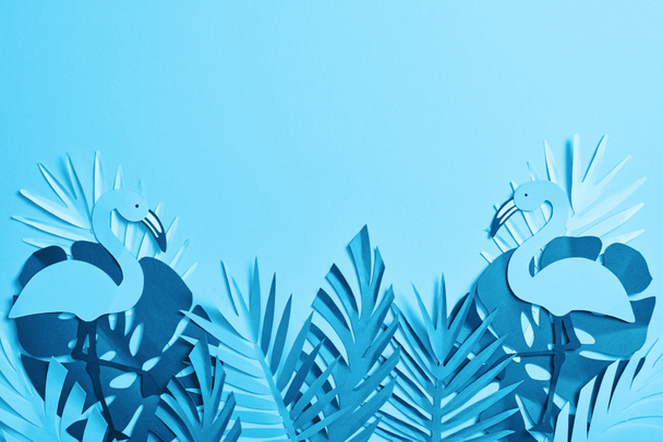 top view of blue paper cut palm leaves and flamingos on blue background with copy space - Photo, Image