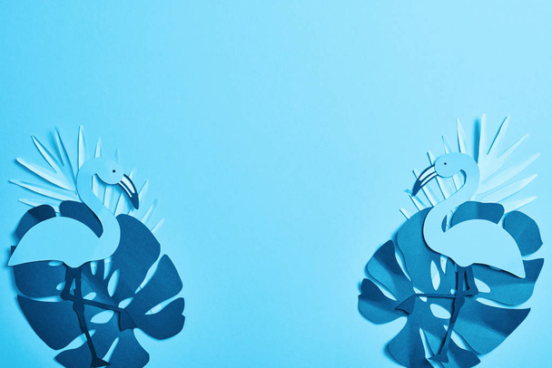Top uitzicht van blauwe exotische papier gesneden Palm bladeren en flamingo's op blauwe achtergrond met Kopieer ruimte - Foto, afbeelding