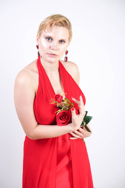 hot blonde caucasian woman wearing long red evening dress and posing on white studio background alone. fashionable adult girl with plus size body standing in stylish party clothes. - Valokuva, kuva