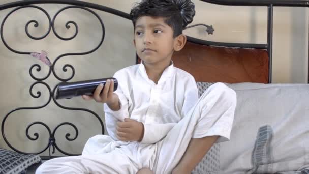 niedlichen indischen asiatischen kaukasischen Jungen Kind ändern tv-Kanal mit Fernbedienung und versuchen, damit es funktioniert, indem Sie es von vorne sehen - Filmmaterial, Video