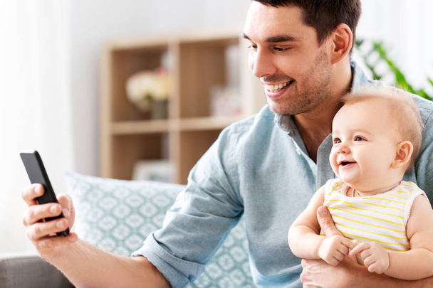 father with baby daughter using smartphone at home - Photo, Image