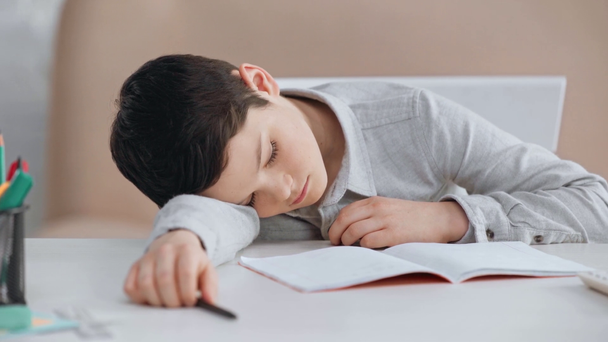 unavený školák s perem na stole poblíž kopírovací knihy, kalkulačky a tužky - Záběry, video