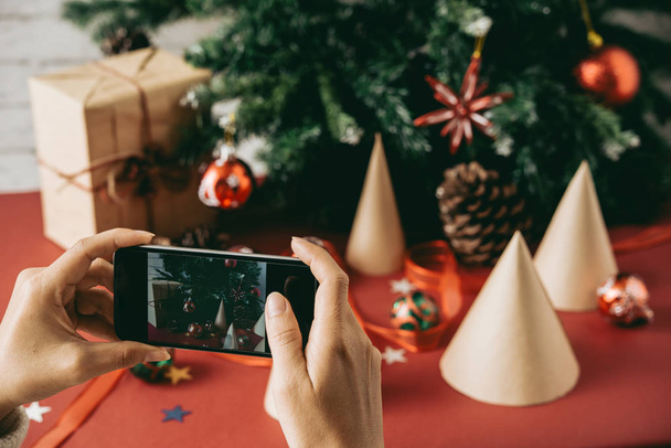 Крупним планом невизначена жінка фотографує різдвяну композицію проти дерева, щоб розмістити її в соціальних мережах
 - Фото, зображення