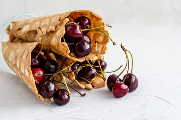Ice cream cone filled with cherries on a light white concrete ba - Foto, Imagem
