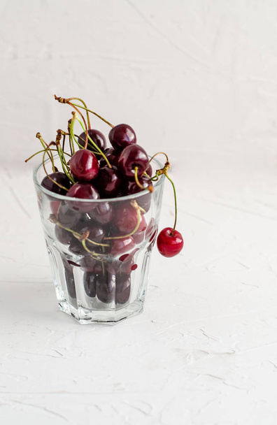Ripe fresh red sweet cherry in a glass beaker on a white concret - Foto, Imagem