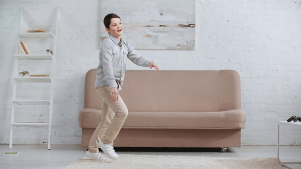 KYIV, UCRAINA - 15 APRILE 2019: veduta completa del bambino sorridente felice che balla sul tappeto vicino al divano in soggiorno
 - Filmati, video