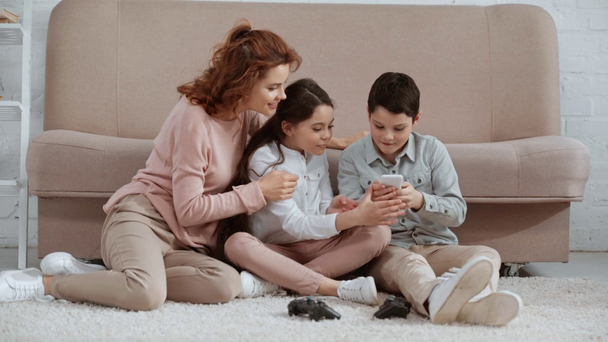 szczęśliwy uśmiechnięta rodzina siedzi na dywanie w pobliżu sofy, biorąc selfie i pokazując kciuk i znaki pokoju - Materiał filmowy, wideo
