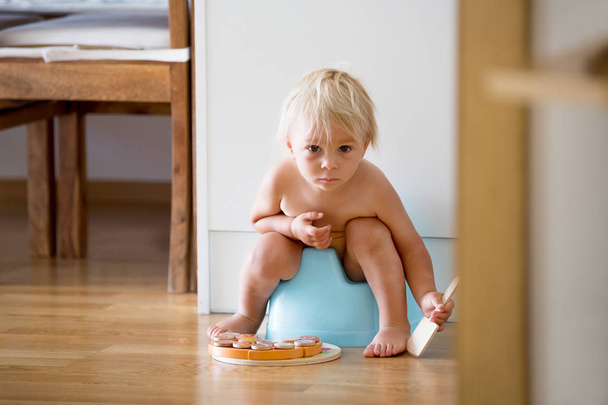 Little toddler boy, sitting on potty, playing with wooden toy - Zdjęcie, obraz