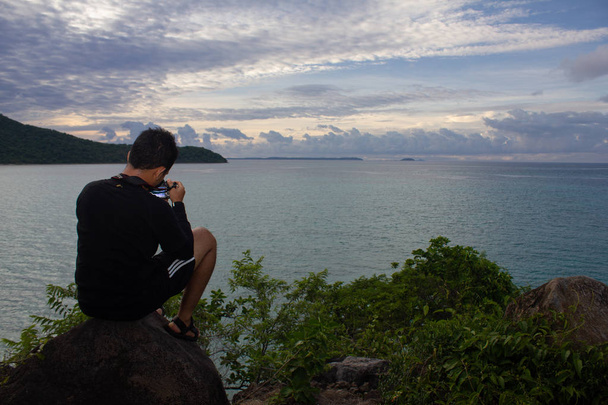 FLORES / INDONESIA-GENNAIO 04 2014: Un fotografo si gode la vista sul mare da una collina. Ha ripreso il momento usando la sua macchina fotografica
 - Foto, immagini